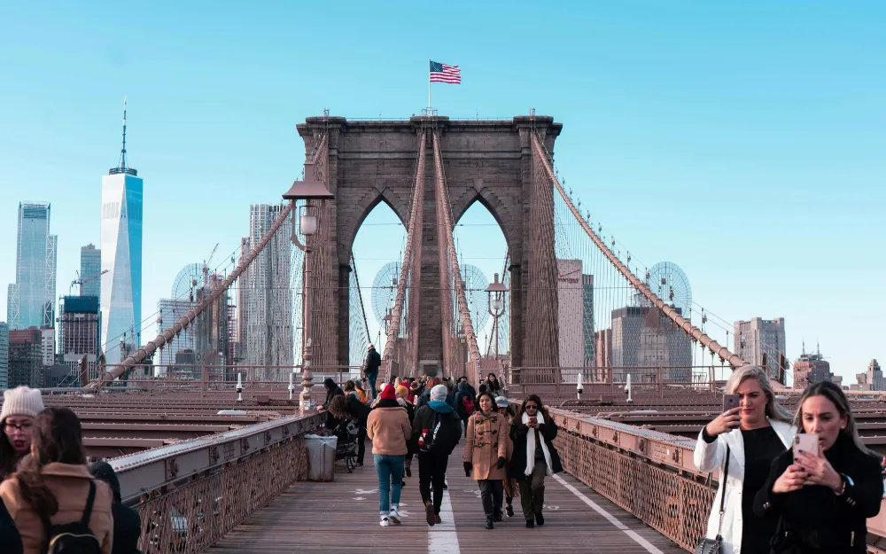 Things to Do in NYC 2 Visitors walking the Brooklyn Bridge pedestrian walkway toward the Lower Manhattan skyline