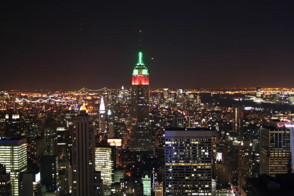 Empire State Building Tickets: Real Prices, the $5 Fee, and Where to Buy 2 The Empire State Building lit at night above the Midtown Manhattan skyline, seen from the Rockefeller Center