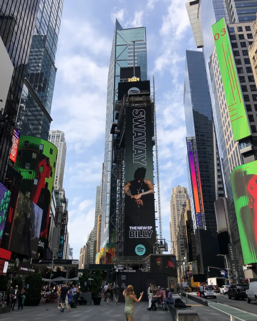 Times Square: Where It Is, What Is Worth Seeing, and How to Do It at Night 2 One Times Square covered in billboards and scaffolding at the southern end of Times Square, seen from the Broadway plaza near 44th Street, with a taller glass tower behind it