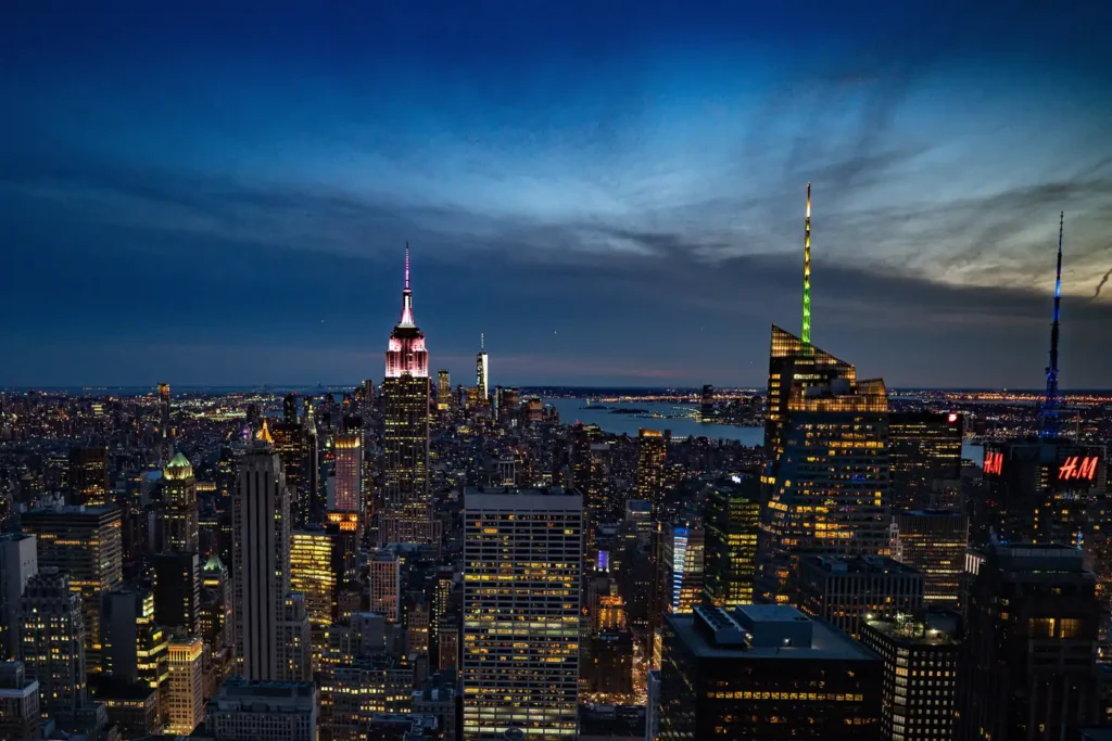 Top of the Rock Tickets: Real Prices, the Free Early Hour, and the Weather Guarantee 1 The Midtown Manhattan skyline at night from the Top of the Rock observation deck, with the Empire State Building lit and One World Trade Center behind it