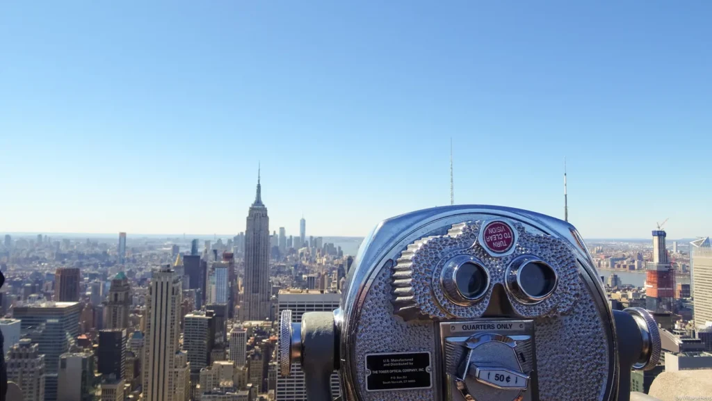 Top of the Rock Tickets: Real Prices, the Free Early Hour, and the Weather Guarantee 2 A coin-operated viewer on the Top of the Rock observation deck, with the Empire State Building and One World Trade Center in the view beyond